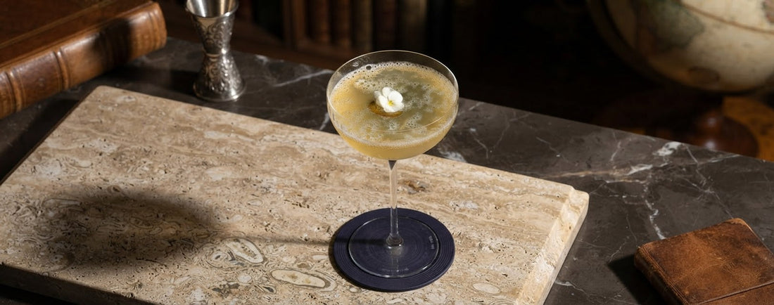 Two pale golden sparkling mocktails made with Chardonnay grape juice, lime, elderflower and jalapeño, served over ice in elegant wine glasses and garnished with green jalapeño slices and edible flowers.