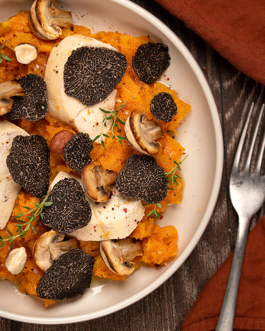Black truffle shaved over a dish of roasted squash, mushrooms and herbs in a cream bowl with a fork