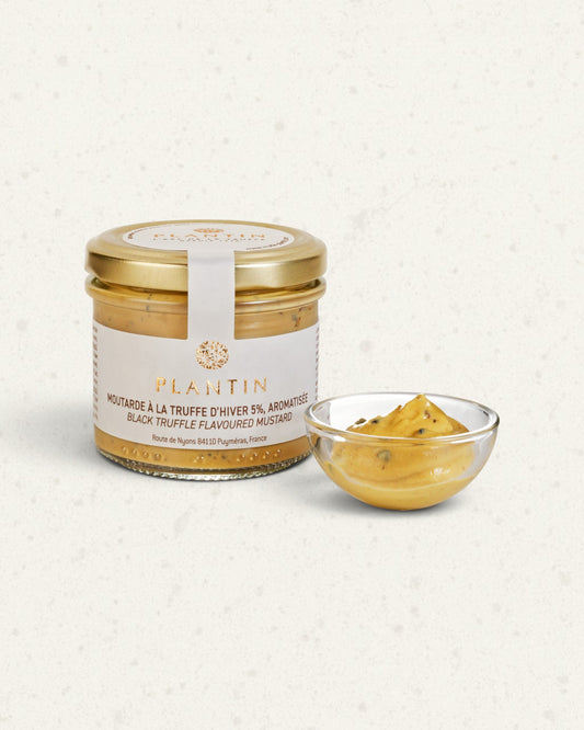 Glass jar of Plantin black truffle mustard with a gold lid, beside a small glass dish of mustard
