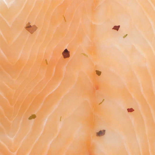 Close-up of smoked salmon slices flecked with herbs and pink peppercorns, showing the pale lines