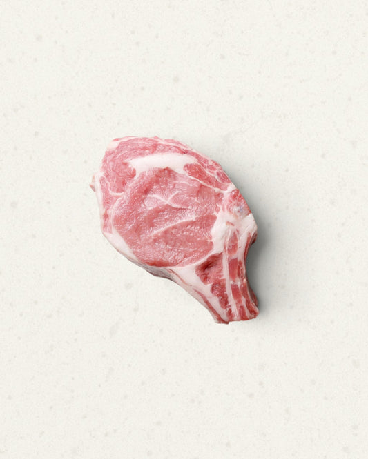 Raw bone-in veal prime rib chop with pale pink meat and a short rib bone, on a light cream background